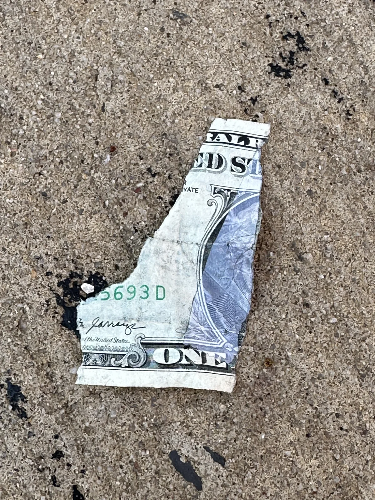 A torn fragment of a dollar bill lying on rough pavement.