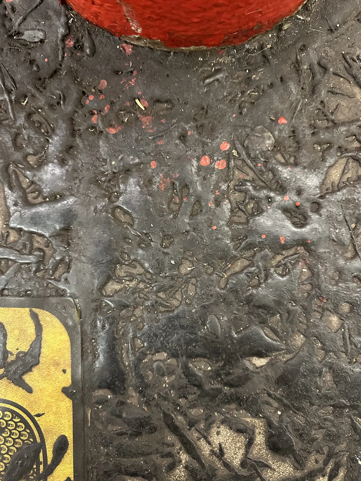 Worn, textured metal with red paint flecks and part of a yellow sticker.