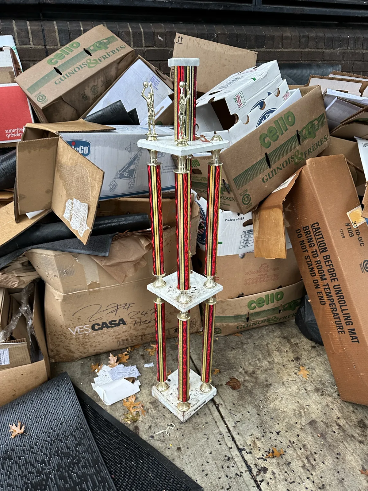 A tall red-and-gold trophy standing among discarded cardboard boxes.