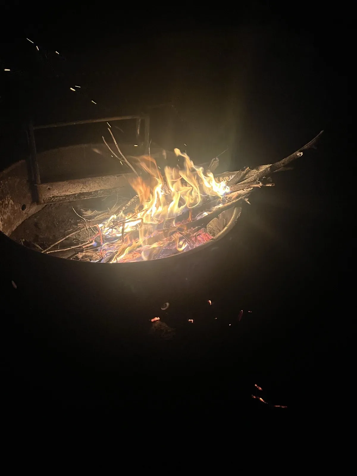 Flames and glowing embers in a metal fire pit at night.